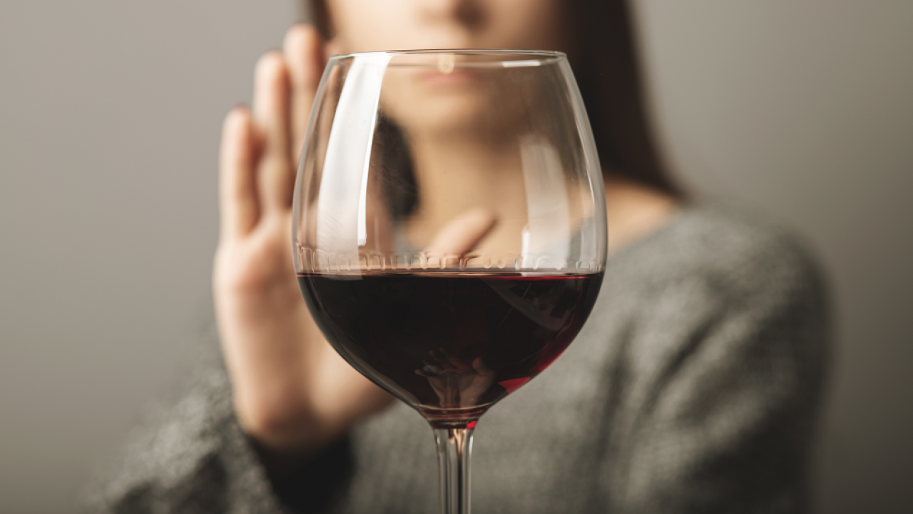 Blurred woman stands behind wine glass with her palm behind it