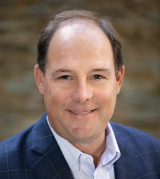 Man in a blue blazer smiling against a blurred stone background.